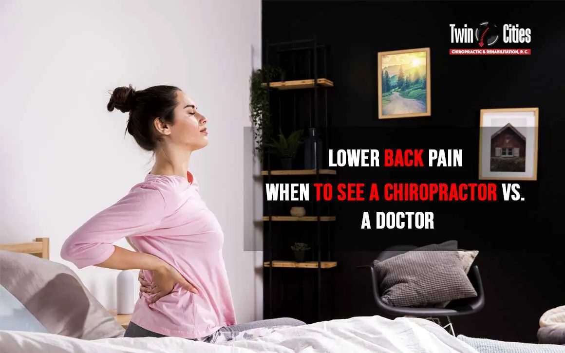 Woman holding her lower back in pain while getting out of bed, considering whether to see a chiropractor or medical doctor at Twin Cities Chiropractic & Rehabilitation.
