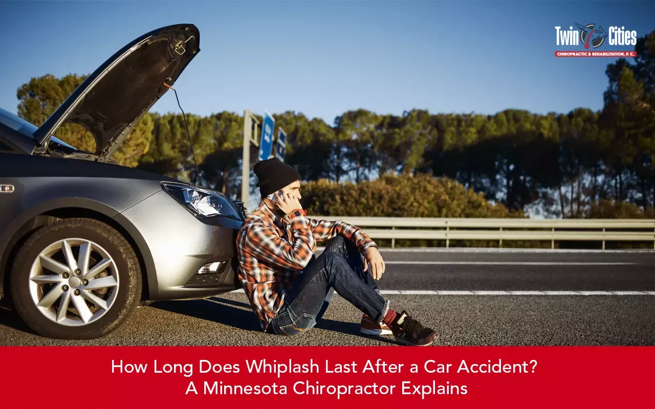 Driver sitting beside a disabled car after a roadside accident, illustrating whiplash injuries and recovery after a car crash.